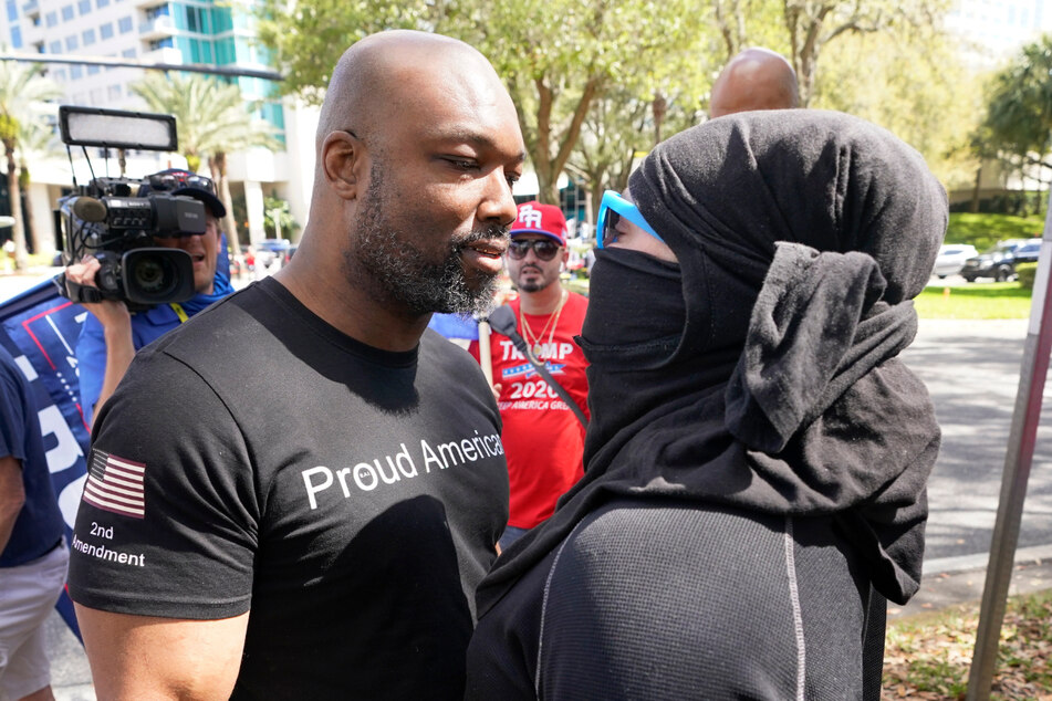 Ein Trump-Anhänger, der ein T-Shirt mit der Aufschrift "Proud American" (Stolzer Amerikaner) trägt, streitet sich vor dem Veranstaltungsort der CPAC mit einer Demonstrantin.