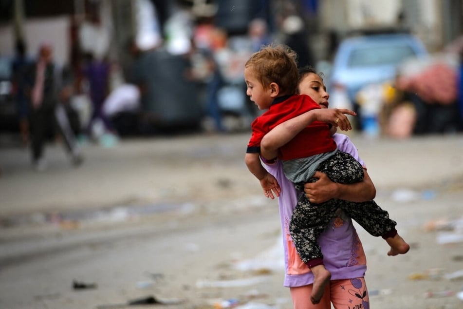 A Palestinian girl carries a toddler as people flee Rafah in the southern Gaza Strip on May 11, 2023.