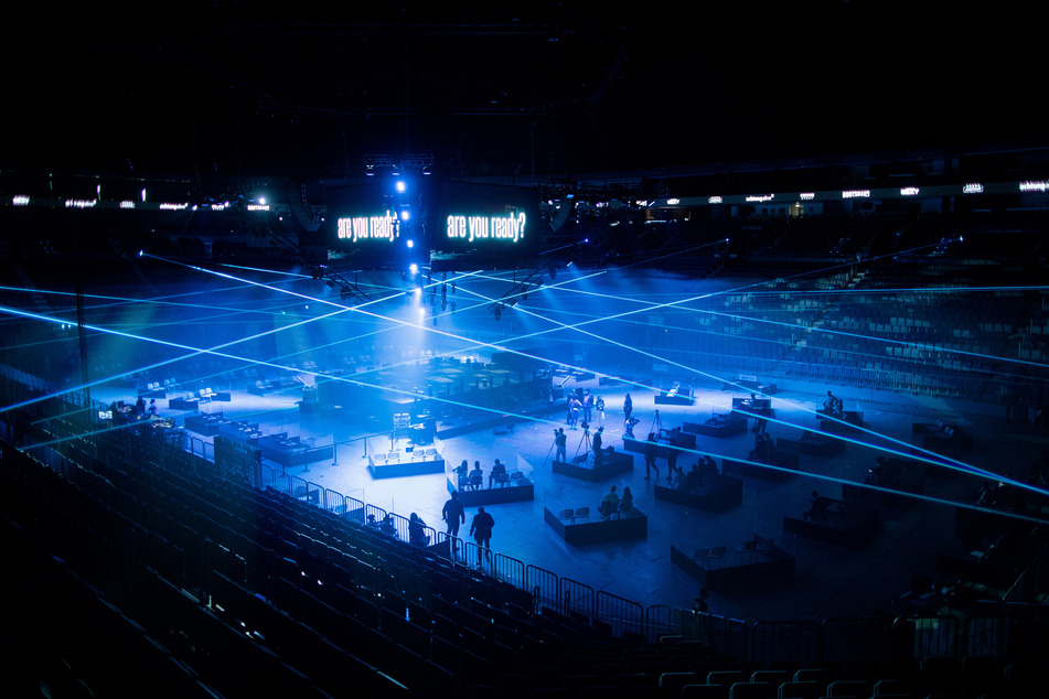 Journalisten und Besucher sitzen bei einem Pressetermin in Boxen aus Plexiglas in der Lanxess-Arena.