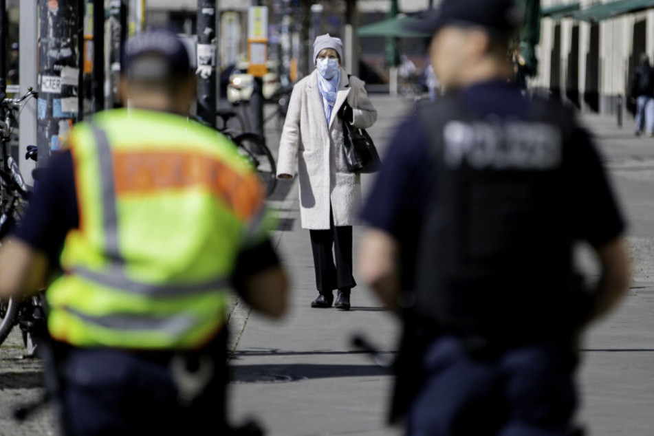 Eine Frau mit Mundschutz kommt am Alexanderplatz zwei Polizeibeamten der Brennpunkt- und Präsenzeinheit (BPE) der Polizei Berlin entgegen.