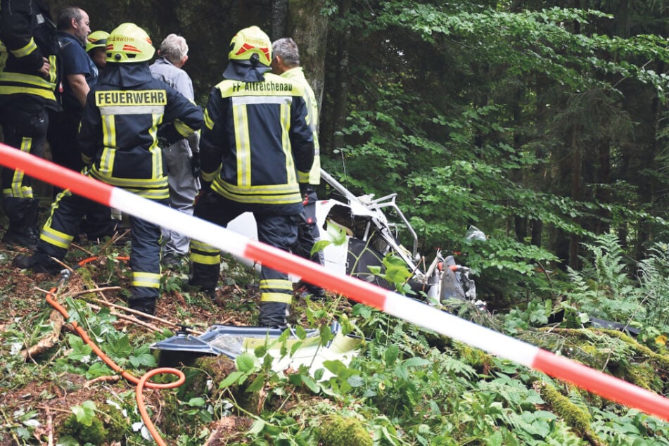 Feuerwehrleute ziehen den abgebrochenen Rumpf des Ultraleichflugzeugs aus dem Wald.