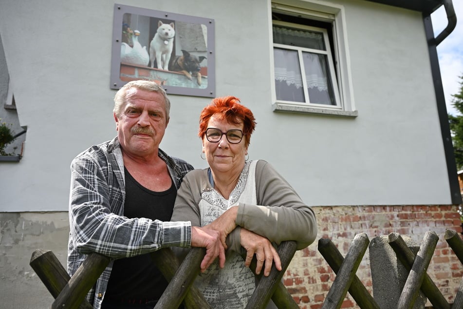 Karin (68) und Gerald Zimmer (61) haben ihr Herz für Schwäne als Bild an der Hauswand. Vor dem Zaun geben sie den Tieren Wasser.