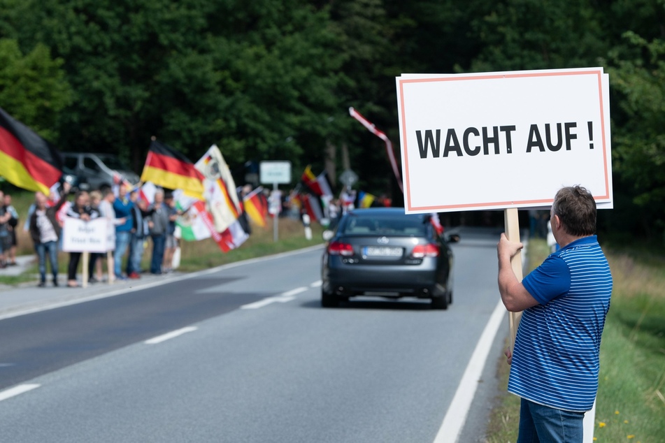 Sachsen, Oppach: Teilnehmer eines Protests stehen mit Fahnen an der Bundesstraße 96. Ein Teilnehmer hält ein Schild mit der Aufschrift "Wacht auf!". (Archivbild)