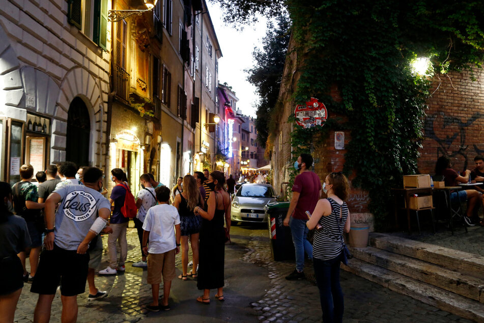 Gäste stehen mit Mundschutzen vor einem Restaurant an. Italiens Regierung bereitet nach Medienberichten eine erneute Verschärfung der Anti-Corona-Maßnahmen vor, um den steilen Anstieg der Ansteckungszahlen zu bremsen.