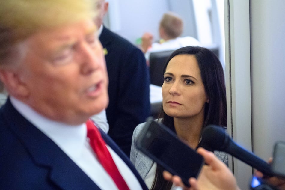 White House Press Secretary Stephanie Grisham listens as President Donald Trump speaks to the media while aboard Air Force One on August 7, 2019.