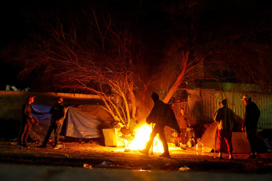 Asylum-seekers, mostly from Venezuela, stand around a campfire near the border between the US and Mexico,