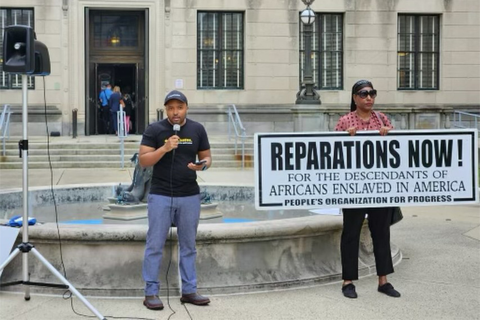 Jean-Pierre Brutus (l.) speaks at a rally in Trenton calling on the state legislature to establish a reparations task force.