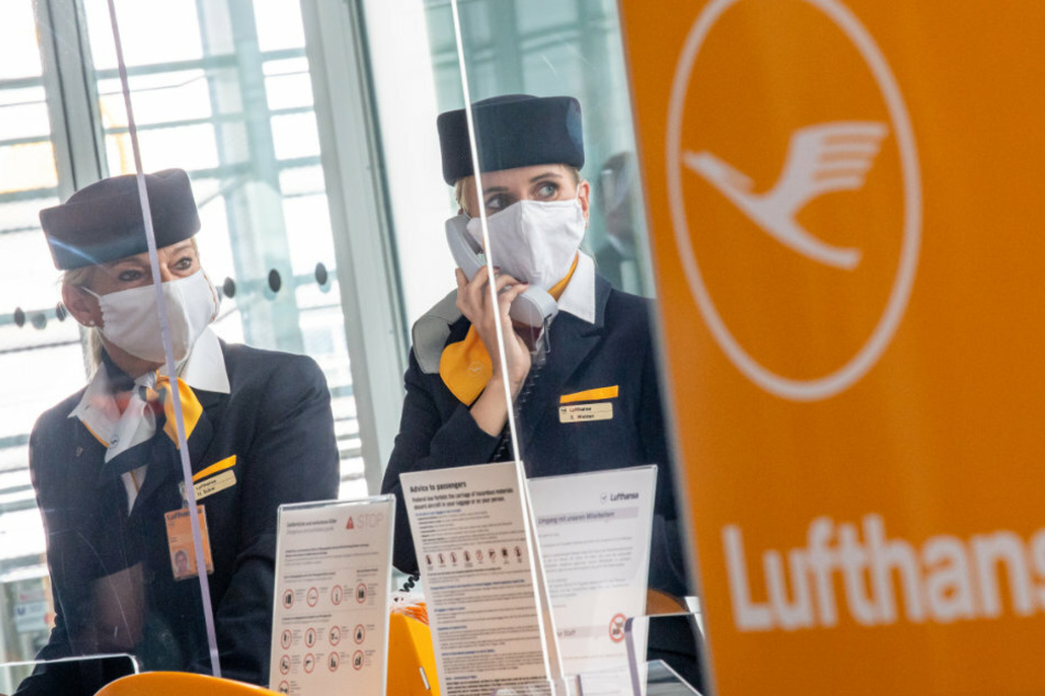 München: Zwei Lufthansa-Mitarbeiterinnen mit Mund-Nasen-Schutzmaske und hinter Plexiglasscheiben fertigen am Flughafen-Terminal 2 die Gäste für den Flug in die USA ab.