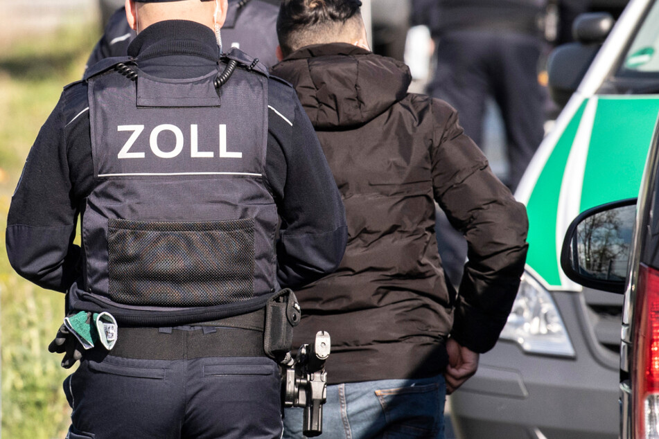 Zollbeamte führen während einer Razzia bei einem Reinigungsunternehmen in Frankfurt einen Mann zur Personalien-Überprüfung.