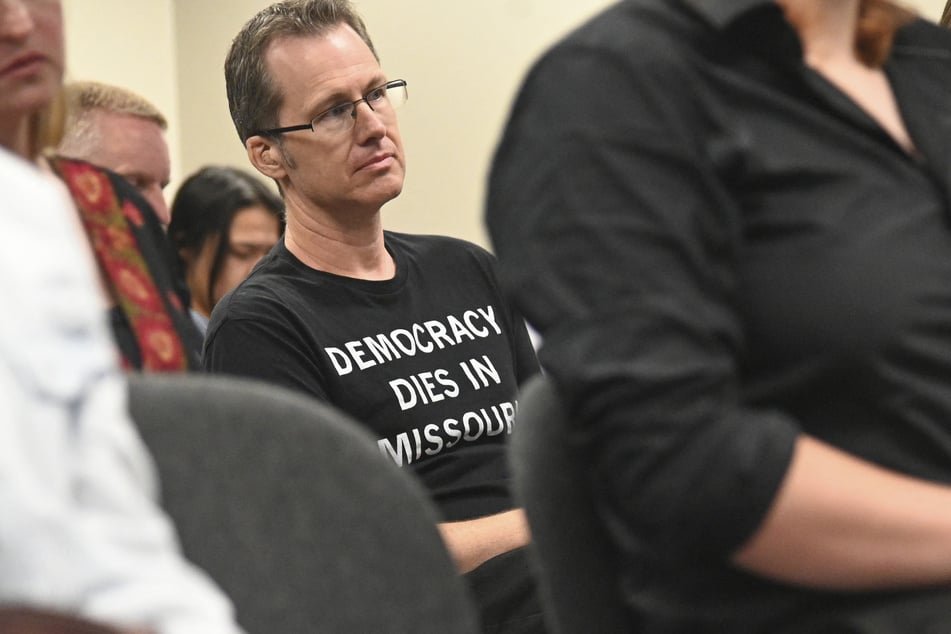 A man wearing a shirt that reads "DEMOCRACY DIES IN MISSOURI" looks on during a special committee hearing on redistricting at the State Capitol in Jefferson City on September 4, 2025.