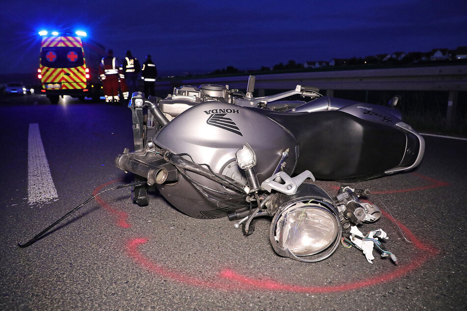 Das demolierte Motorrad liegt auf der Straße, während im Hintergrund der Rettungswagen zu sehen ist.