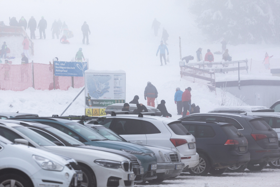 Oberried: Menschen stehen im dichten Nebel nahe dem Skilift am Haldenköpfle, während im Vordergrund der volle Parkplatz der geschlossenen Liftanlage zu sehen ist.
