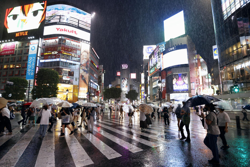 Menschen mit Regenschirmen gehen über eine Straße im Stadtteil Shibuya in Tokio.