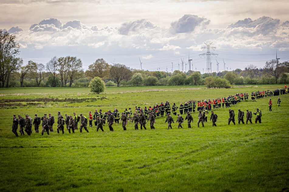 Soldaten der Bundeswehr und Einsatzkräfte der Feuerwehr stellen sich auf, um ein Feld abzusuchen. (Archiv)
