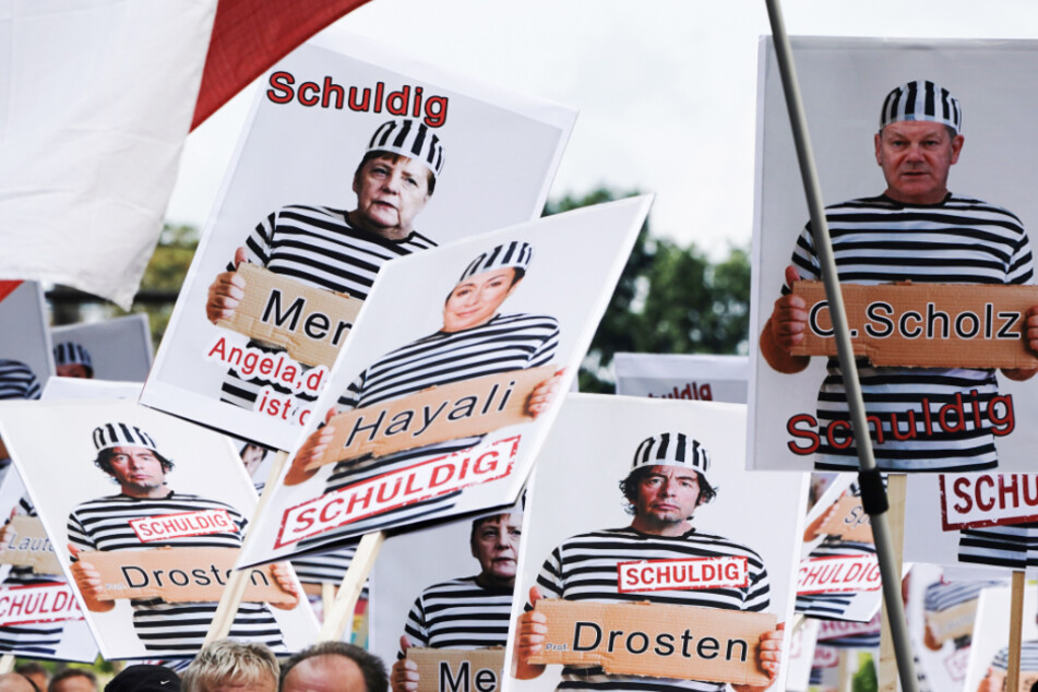 Plakate von Politikern, Virologen und TV-Journalisten in Knast-Kleidung.