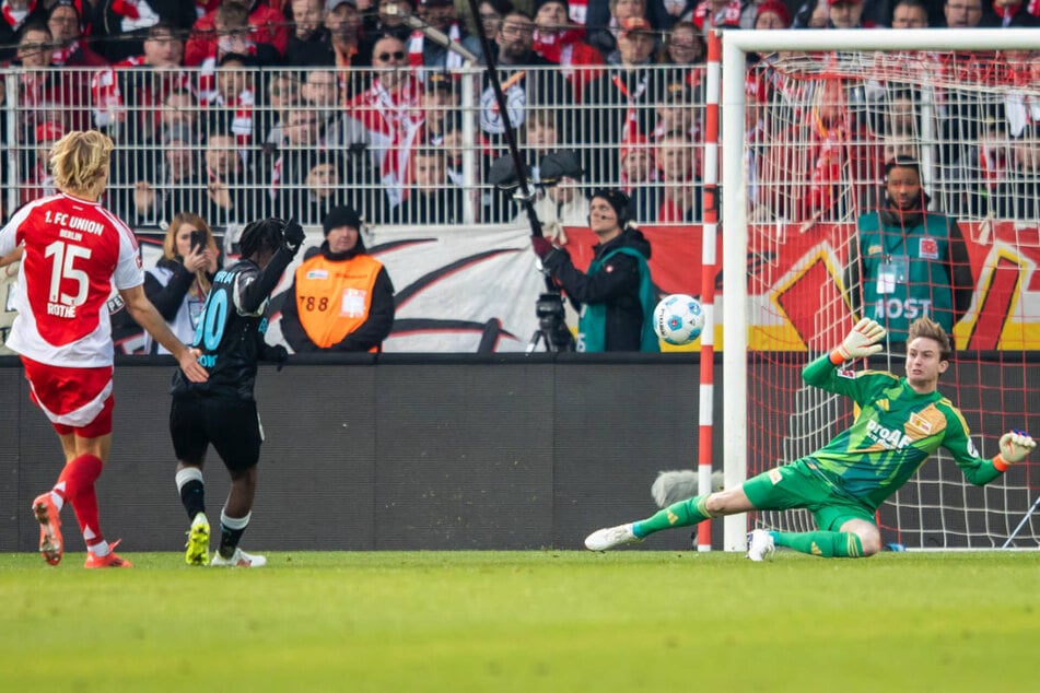 Jeremie Frimpong (M.) schiebt zur Bayer-Führung ein - Tom Rothe (l.) und Keeper Frederik Rönnow haben das Nachsehen.