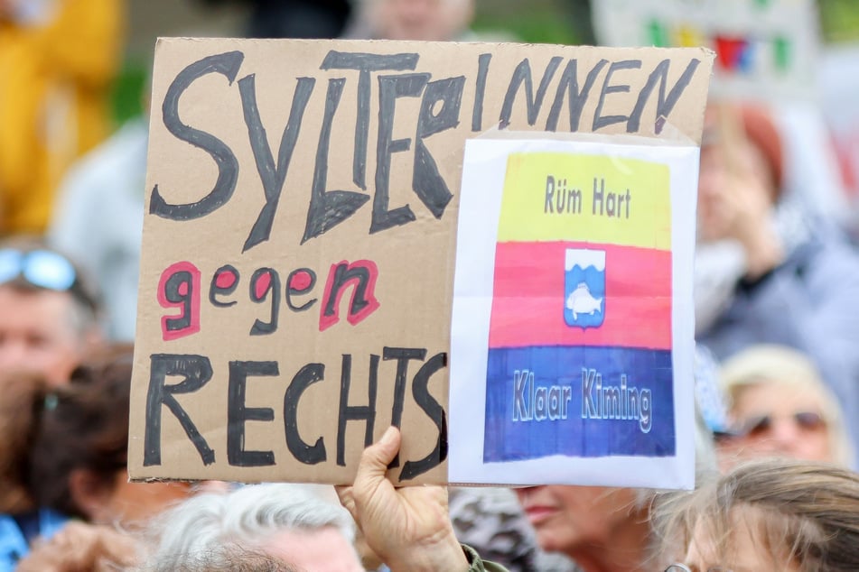 Teilnehmer halten bei einer Kundgebung Pappschilder hoch, darunter ein Schild mit dem Schriftzug "SylterInnen gegen rechts".