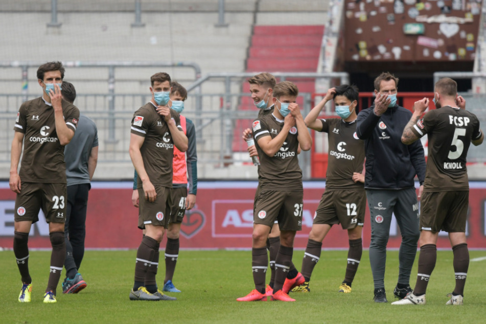 St. Paulis Spieler stehen mit Maske auf dem Rasen.