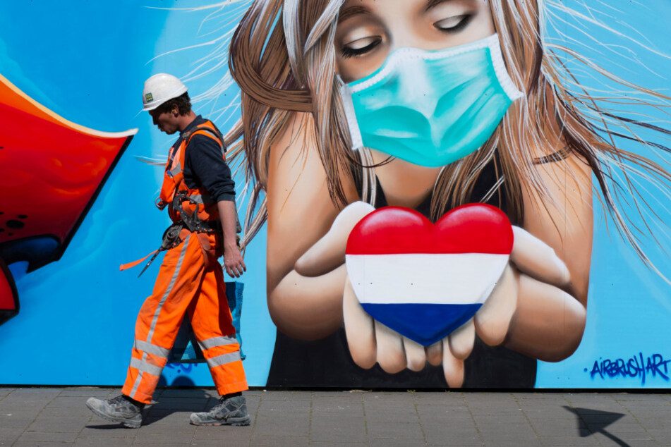 Ein Bauarbeiter geht in Den Haag an einem Wandbild des Künstlers Casper Cruse vorbei, das eine Frau mit einer Gesichtsmaske zeigt, die ein Herz in den Farben der niederländischen Flagge hält, als Zeichen der Unterstützung für diejenigen, die unter den Auswirkungen des Coronavirus leiden.