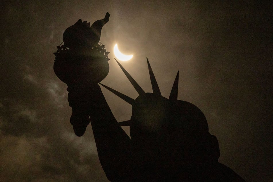 Der Mond verdeckt teilweise die Sonne hinter der Freiheitsstatue auf Liberty Island.