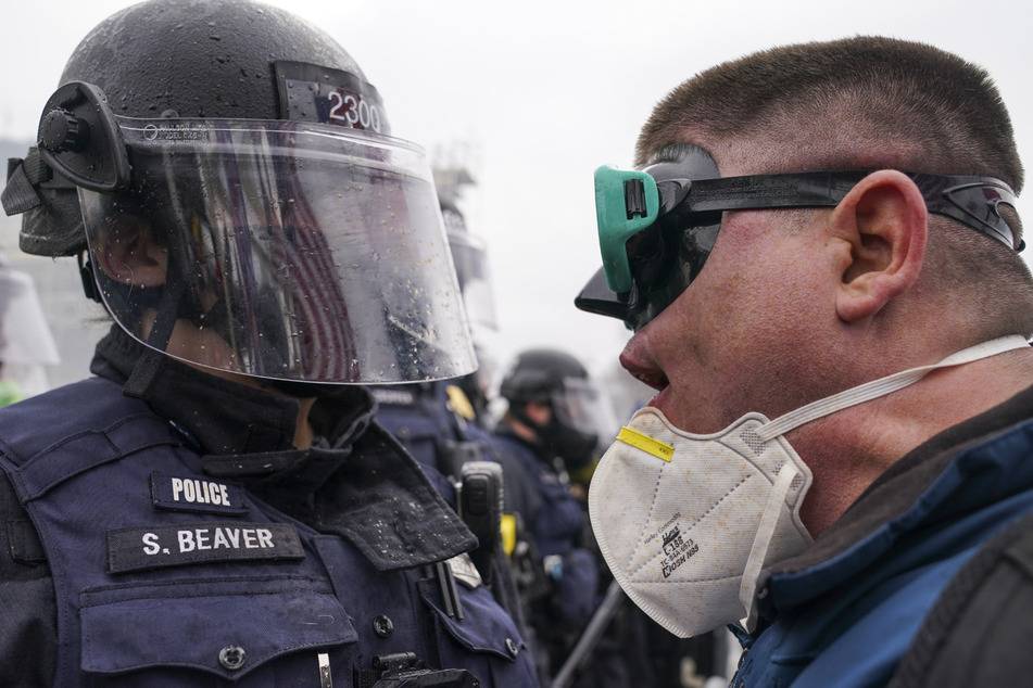 Auge in Auge und voller Hass: Ein Polizist mit völlig besudeltem Visier stellt sich einem Demonstranten gegenüber.