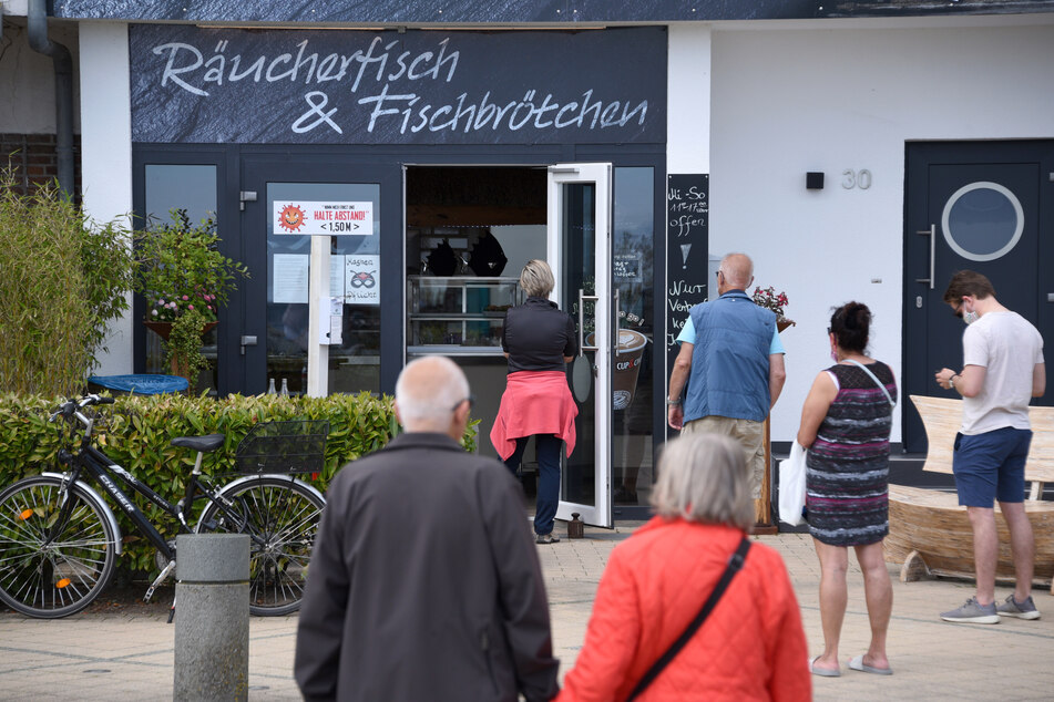 Gäste stehen mit Abstand vor einem Fischgeschäft in Schleswig-Holstein.