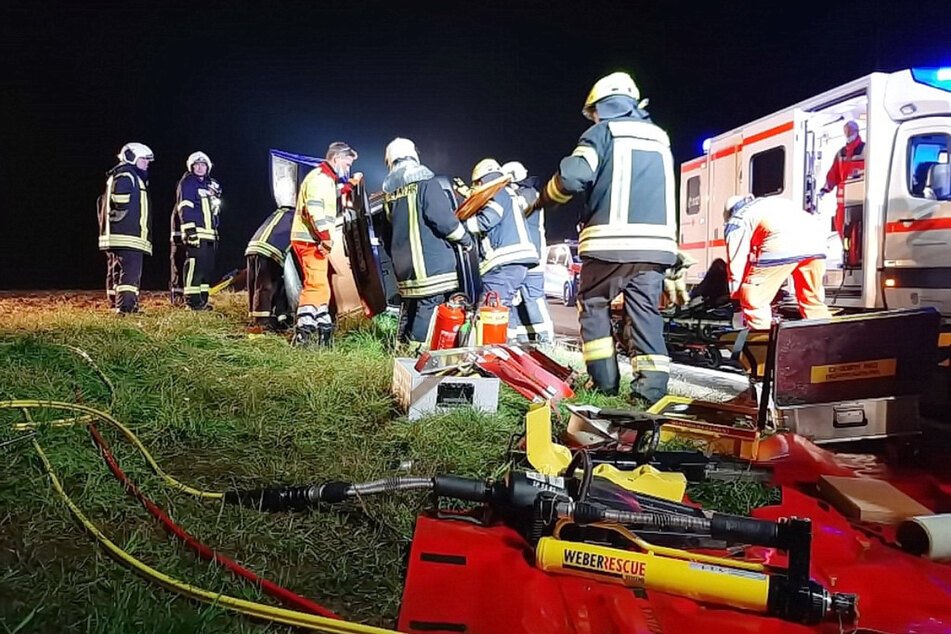 Die Feuerwehr versucht den Fahrer aus seinem Auto zu befreien. Daneben steht bereits der Rettungsdienst mit einer Trage.