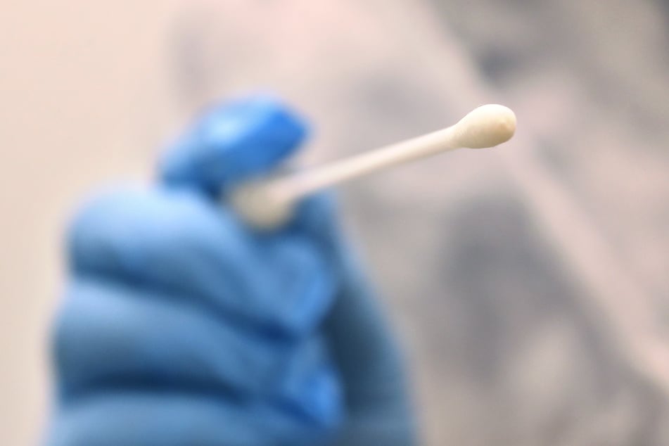 Ein Arzt hält in einer Hausarztpraxis einen Tupfer mit dem ein Abstrich für einen Coronatest gemacht wird.