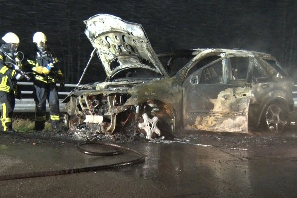 Feuerwehrleute stehen neben dem ausgebrannten Auto auf der Bundesstraße 408.