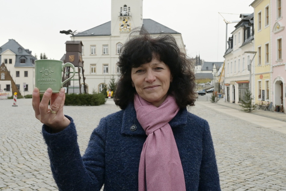 Heidi Schmidt, Sachgebietsleiterin für Tourismus- und Wirtschaftsförderung in Schneeberg, zeigt die nagelneue Tasse. Diese wurde in Sachsen gefertigt.
