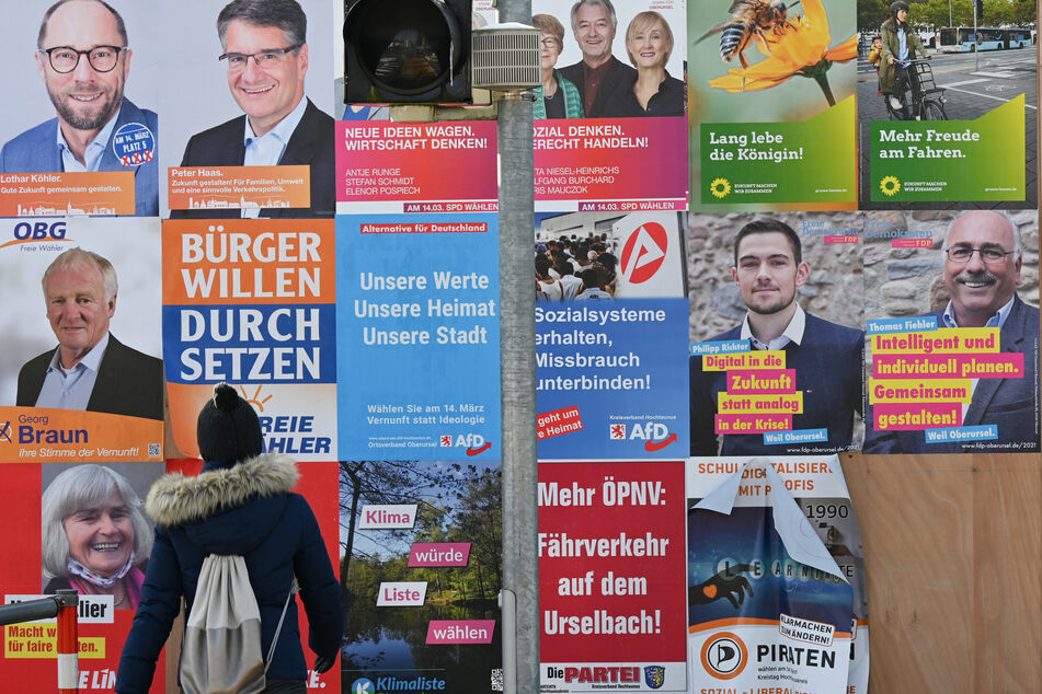 Mit Wahlplakaten werben verschiedene Parteien an einer Plakatwand in Oberursel um die Stimmen bei der Kommunalwahl.