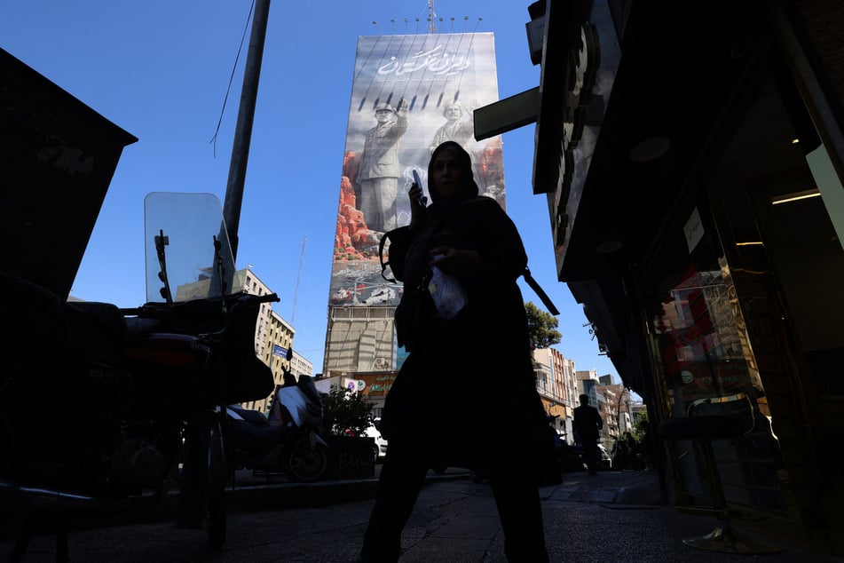 A woman walks along a busy street near a huge mural painted on the side of a building referring to the Strait of Hormuz, in the Iranian capital of Tehran on May 9, 2026.