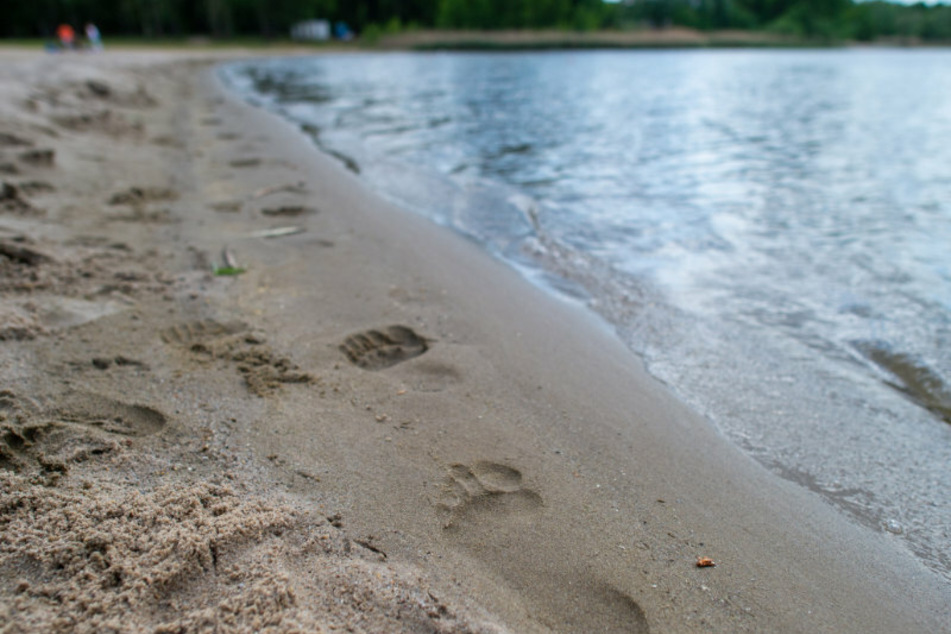 Der Abdruck eines baren Fußes ist im Sand eines Strandbades zu sehen. (Symbolbild)