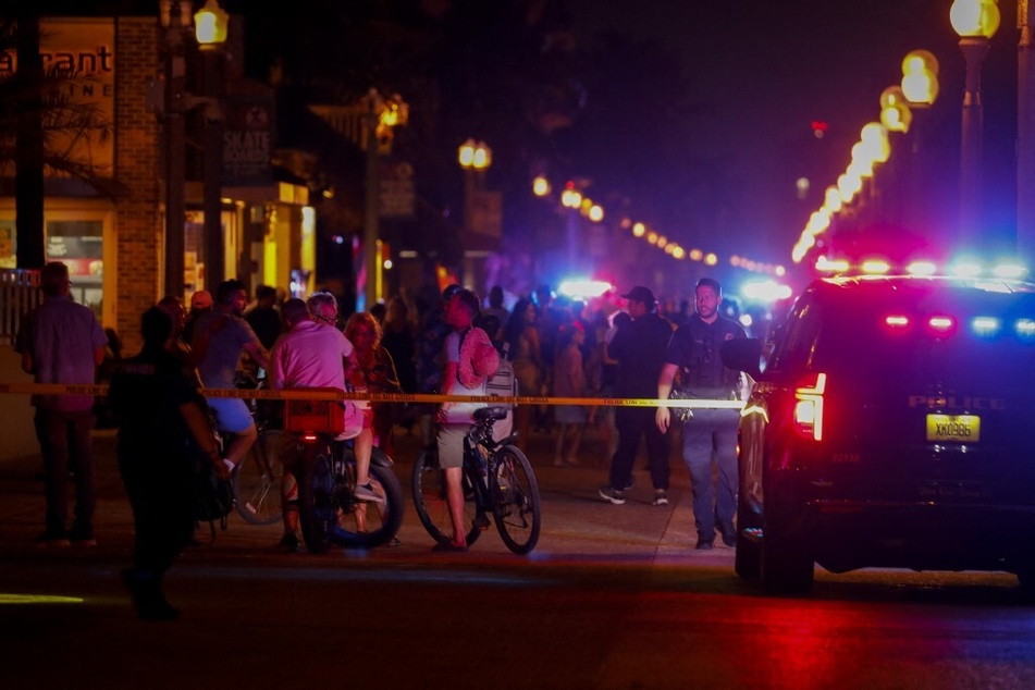 Beachgoers are seen next to law enforcement officers at a crime scene as they respond to a shooting at Florida's Hollywood Beach on May 29, 2023.