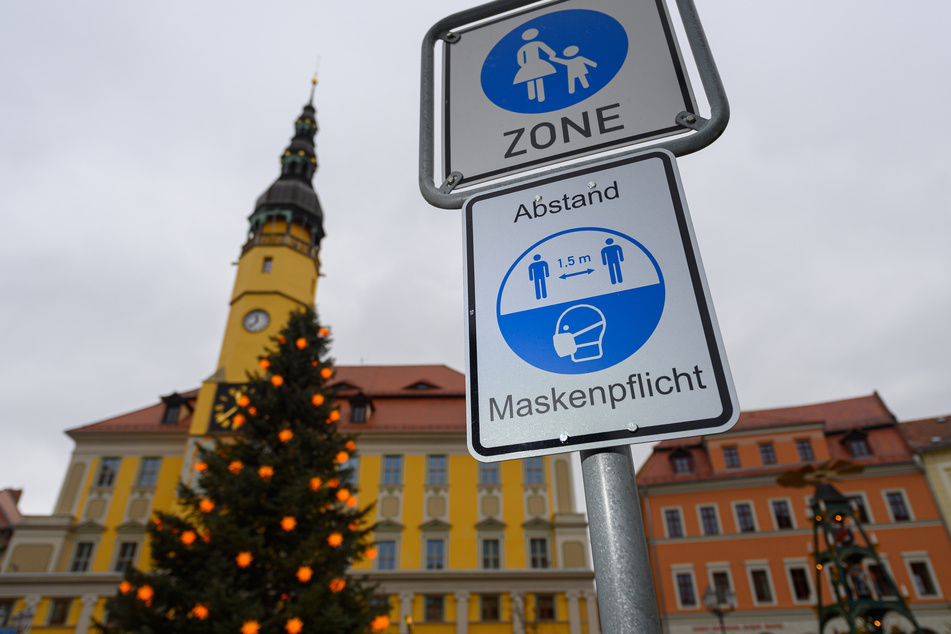 Sachsen, Bautzen: Ein Hinweisschild für die Maskenpflicht und den Abstand ist am Marktplatz vor dem Rathaus, einem Weihnachtsbaum und einer Pyramide zu sehen.