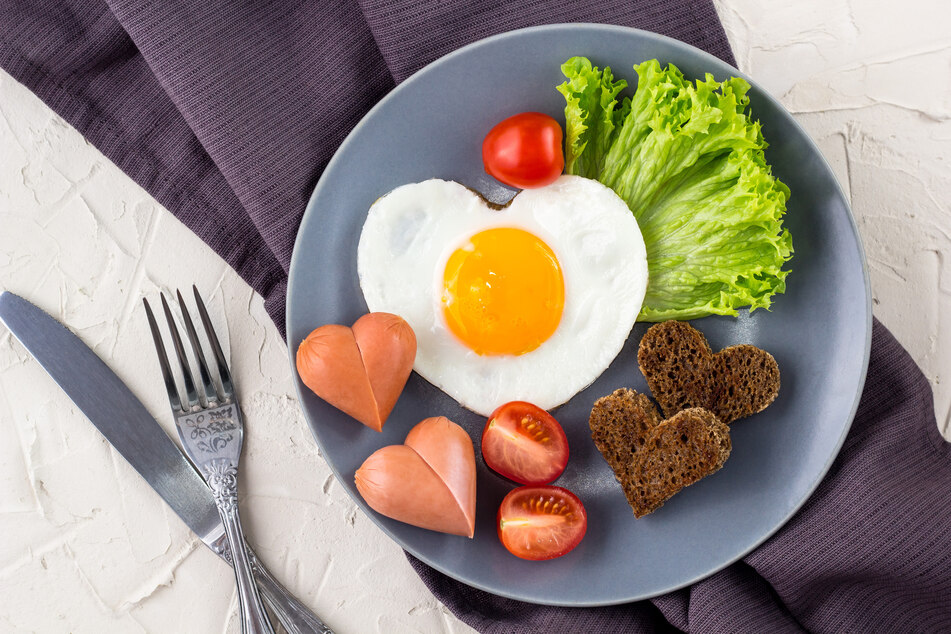 Eine Idee zum Frühstück am Valentinstag ist Spiegelei mit Toast und Würstchen in Herzform.