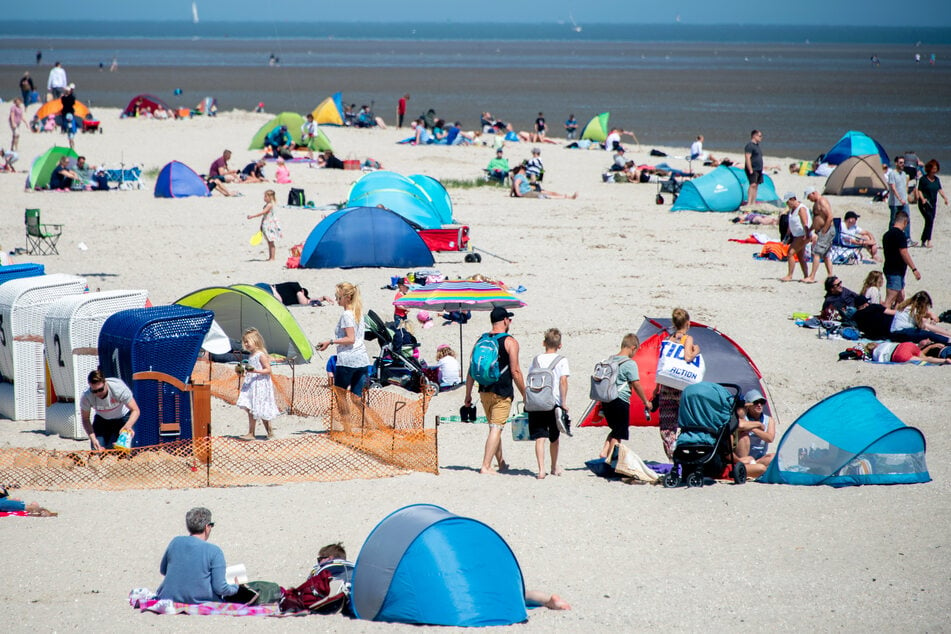 Zahlreiche Touristen sitzen am Strand des Ortes Schillig im Landkreis Friesland.