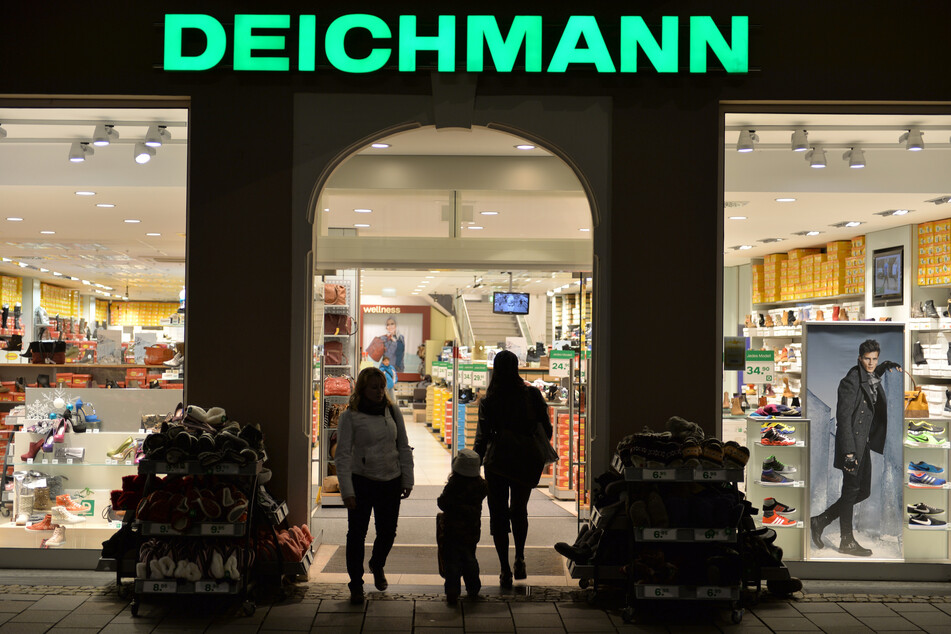Eine Frau geht mit einem Kind in eine Deichmann-Filiale, während eine Kundin aus dem Geschäft geht.
