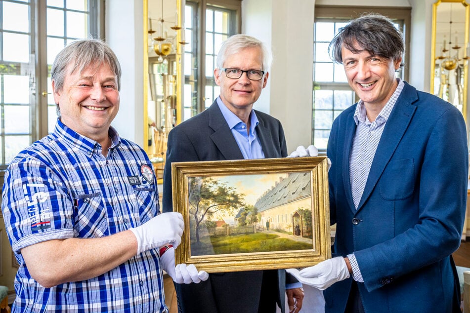 Mitarbeiter Andrej Pawluschkow (l.) und Festungs-Chef André Thieme (r.) nehmen von Christoph Großpietsch, dem Enkel von Kunstsammler Fritz Busche das Gemälde "Ansicht der großen Kaserne auf der Festung Königstein" entgegen.