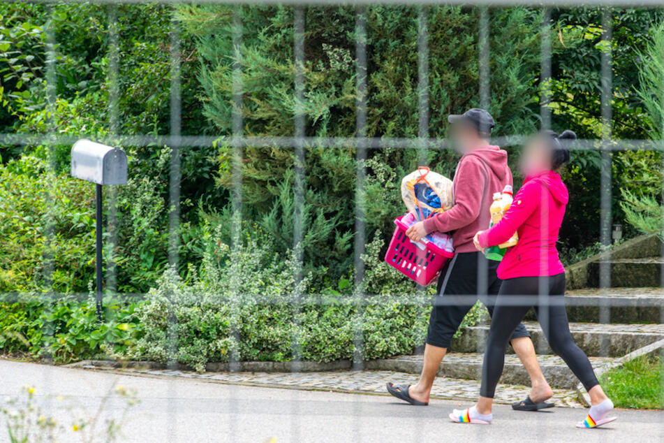 Eine Frau und ein Mann gehen hinter einem Absperrzaun auf dem Gelände eines Bauernhofs. Nach der Masseninfektion stehen fast 500 Menschen unter Quarantäne und dürfen das Betriebsgelände nicht mehr verlassen.