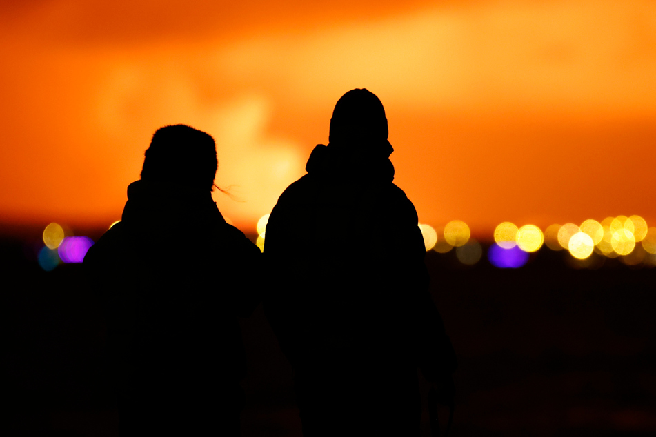 Menschen beobachten, wie der Nachthimmel nach dem Ausbruch eines Vulkans auf der Halbinsel Reykjanes erhellt wird.