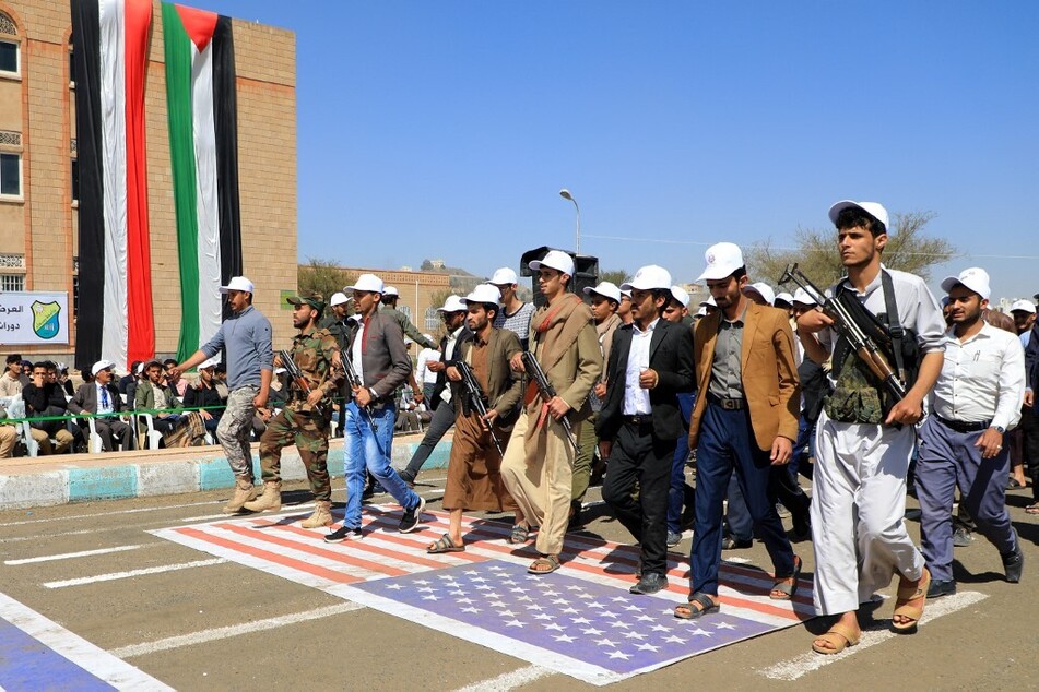 Students recruited into the ranks of Yemen's Houthis parade over a giant US flag during a rally in support of Palestine.