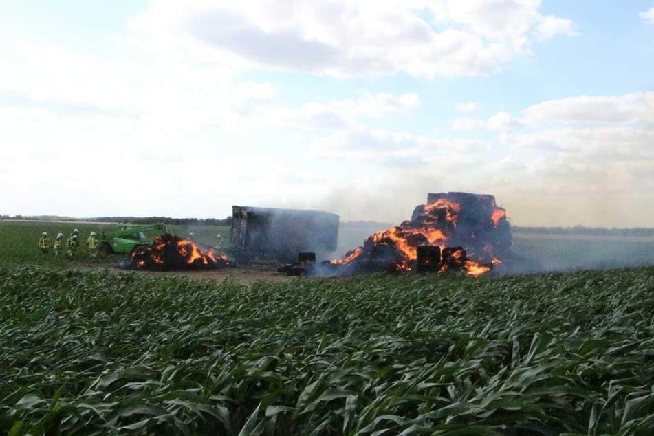 Mehrere Heuballen und ein Anhänger stehen in Flammen.