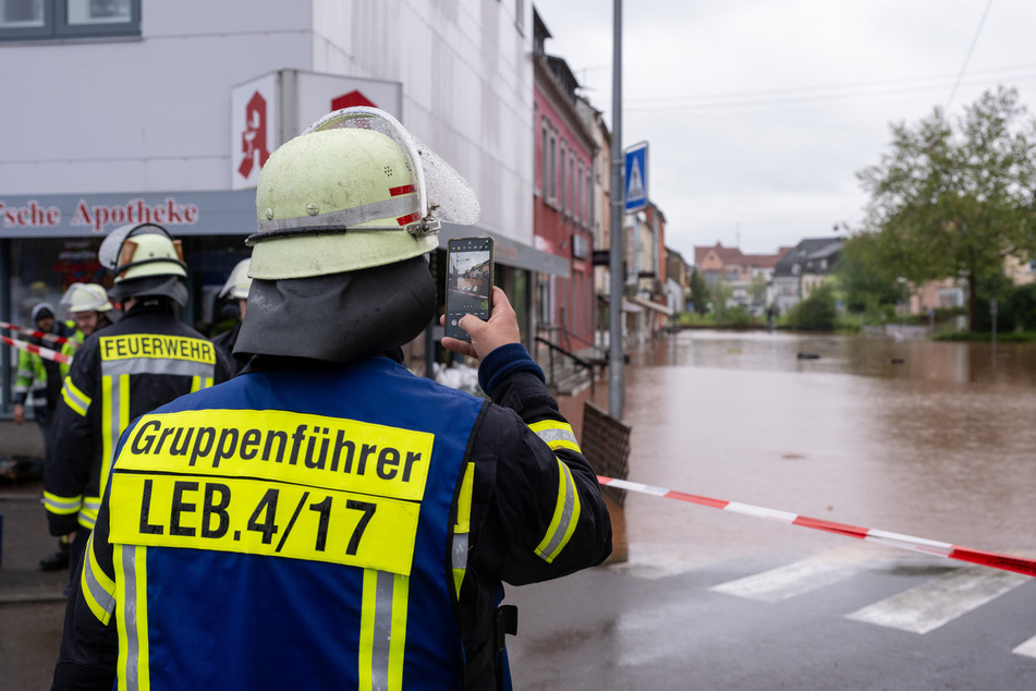 Ein Feuerwehrmann fotografiert das Hochwasser der Theel in der Innenstadt von Lebach.