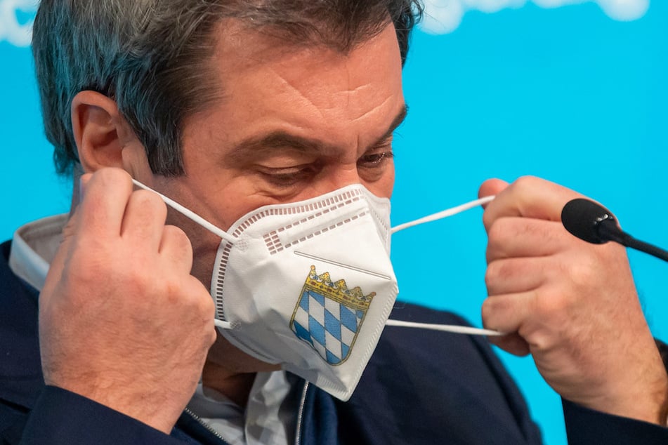 Markus Söder (CSU), Ministerpräsident von Bayern, nimmt sich vor Beginn einer Pressekonferenz eine FFP-2 Maske, die mit dem bayerische Staatswappen auf der Vorderseite bedruckt ist, vom Gesicht ab.