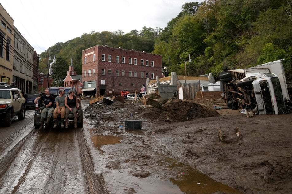 People ride in the back of a pickup truck on a muddy road through the town of Marshall.