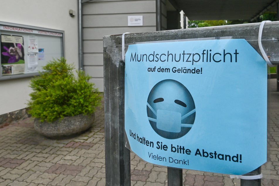 Ein Schild vor einer Schule fordert zum Tragen einer Maske auf.
