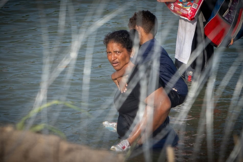 A woman holds a child on her back as migrants walk near concertina wire in the water along the Rio Grande border with Mexico in Eagle Pass, Texas.