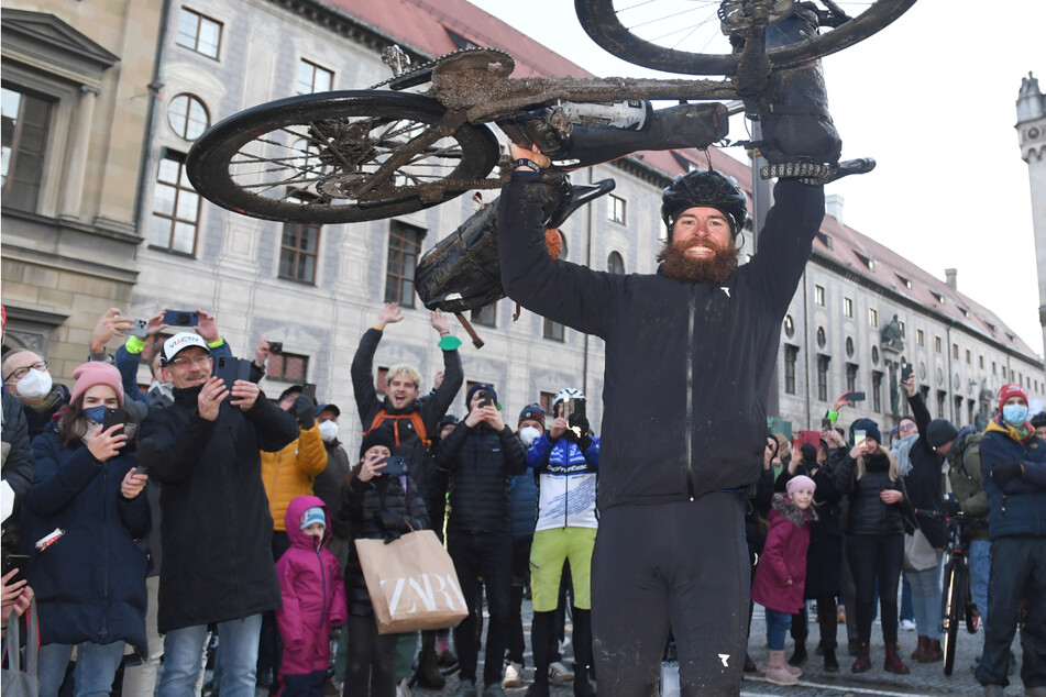 Der deutsche Extremsportler Jonas Deichmann hebt am Odeonsplatz im Ziel seines Triathlon um die Welt sein Fahrrad in die Höhe.