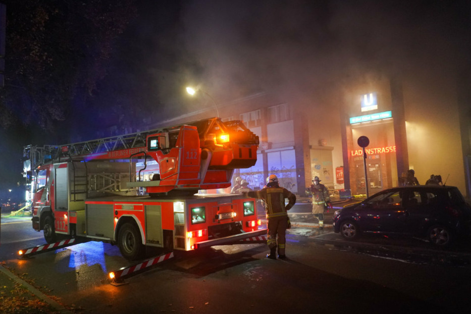Einsatzkräfte der Feuerwehr löschen einen Brand in der Ladenzeile des U-Bahnhofs Onkel Toms Hütte.